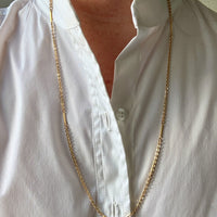 Gold chain necklace worn by a person in a white shirt.