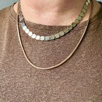 Close-up of a person wearing a gold hexagonal link necklace on a plain background