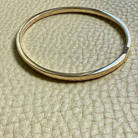 14k Gold solid round bangle on a beige textured surface
