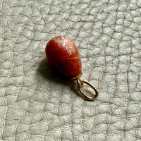 Sunstone teardrop pendant on a gold ring against a gray background