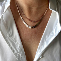 Close-up of a person wearing two gold necklaces with a white shirt.