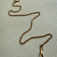 18k Gold antique watch chain necklace on a light gray textured surface