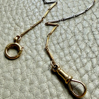 18k Gold and platinum watch chain with clip on a textured beige background