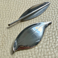 Two Danish vintage sterling silver leaf-shaped brooches on a textured beige surface