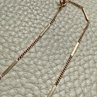 vintage 18k Gold bar and curb link necklace on a textured light gray background