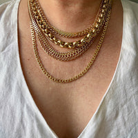 A close-up of a person wearing a layered stack of 18k gold chain necklaces over a white V-neck top.
