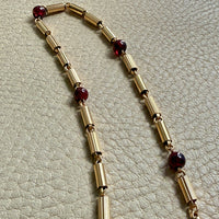 Gold necklace with red beads on a textured beige surface