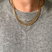 A close-up of a person wearing a double-layered gold chain necklace over a gray knit crewneck sweater.