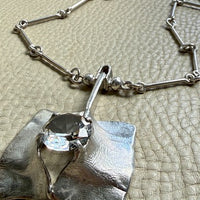 Silver necklace with a unique pendant on a textured surface