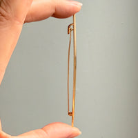 Gold brooch held between two fingers against a gray background