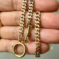Gold watch chain necklace with bolt ring held between fingers against a neutral background