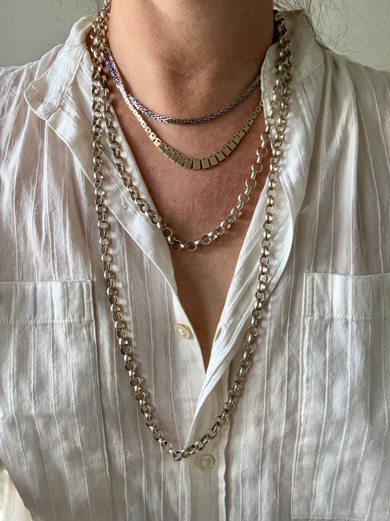 Close-up of a person wearing multiple necklaces with a white shirt.