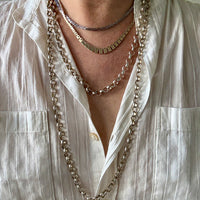 Close-up of a person wearing multiple necklaces with a white shirt.
