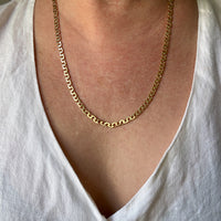 A close-up of a person wearing an 18k gold virola link chain necklace over a white linen V-neck top.