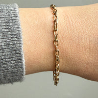 14k Gold vintage biker chain bracelet on a wrist with a gray sleeve against a neutral background
