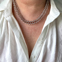 Person wearing a silver chain necklace with a white shirt.