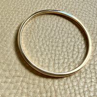 14k Gold solid round bangle on a beige textured surface