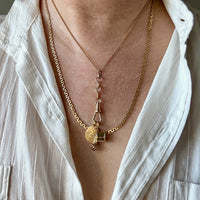 Close-up of a person wearing a gold necklace with a pendant, against a neutral background. Penelope Penelope Vintage Jewelry