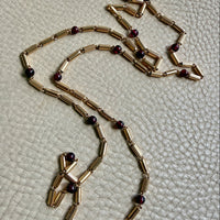 18k Gold necklace with red beads on a textured beige surface