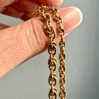 Gold chain held between fingers against a gray background