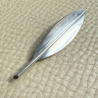 Sterling silver leaf-shaped brooch on a textured beige surface