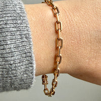 18k Gold biker link chain bracelet on a wrist with a neutral background