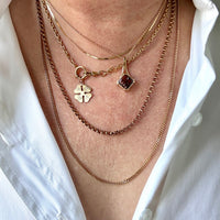 Close-up of layered gold necklaces with heart and clover pendants on a white shirt.