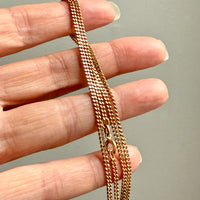 Gold chain held between fingers against a neutral background