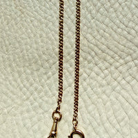 18k gold watch chain necklace with dog clip on a textured light gray background