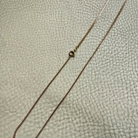 Gold chain necklace on a textured beige surface