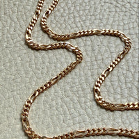 18k Gold figaro link chain necklace on a textured light gray surface