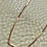 vintage 18k Gold bar and curb link necklace on a textured light green surface
