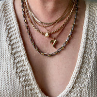 Necklace with gold and silver chains on a person wearing a beige sweater.