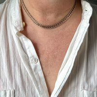A close-up of a person's neck and upper chest wearing a textured, chain-link style gold necklace over a white button-down shirt.