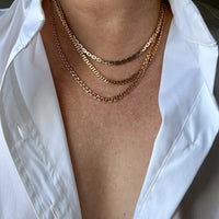 Person wearing gold chain necklaces under a white shirt.