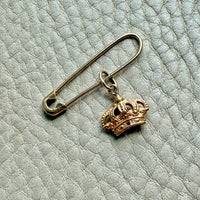 Gold safety pin with a crown charm on a textured light blue background