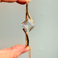 Gold pendant with a clear crystal held by a hand against a light gray background