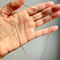 Gold chain held in a hand against a gray background