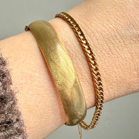 Gold bracelet on a wrist with a neutral background