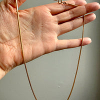 Gold chain held by a hand against a neutral background