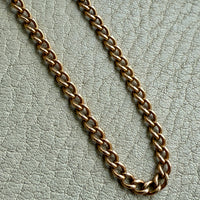 Gold curb chain on a textured light gray background
