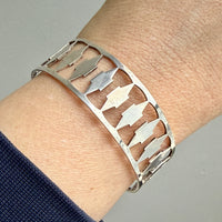 Silver bracelet with cut-out design on a wrist against a neutral background