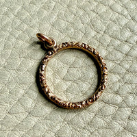 18k Gold ring-shaped pendant on a textured light green background