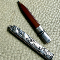 Silver art nouveau pencil case with intricate designs on a textured beige surface