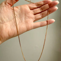 Gold chain held by a hand against a neutral background