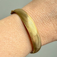 Gold bracelet on a wrist with a plain background