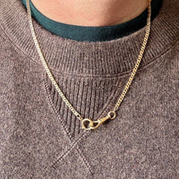 Gold chain necklace worn by a person in a brown sweater with a green shirt underneath.