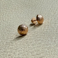 Gold stud earrings on a light gray textured surface