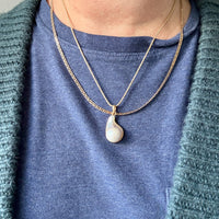Person wearing a blue shirt and green cardigan with a gold necklace featuring a pearl pendant.