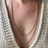 Close-up of a person wearing a gold necklace with a beige knitted sweater. Penelope Penelope vintage 18k gold fine jewelry